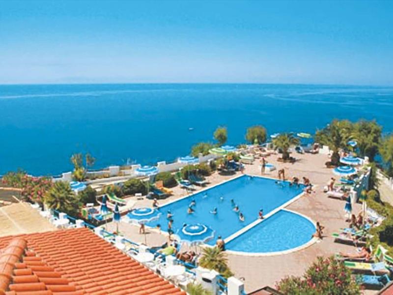 Grande piscine extérieure surplombant la mer, entourée de terrasses ensoleillées et de transats.