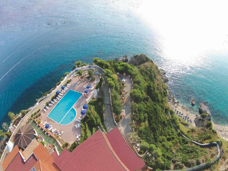 Vue aérienne d'un hôtel avec piscine surplombant la mer en bord de côte.
