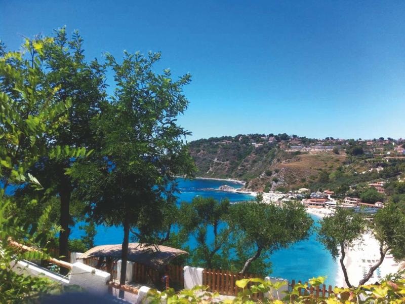 Vue sur une baie avec une eau bleue claire, entourée de collines et d'arbres verts.