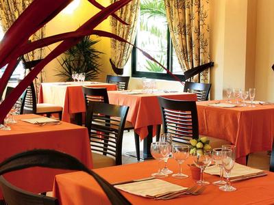 Příjemná jídelna s oranžovými ubrusy, prostřenými stoly a rostlinami u okna.