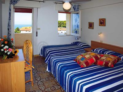 Hotelzimmer mit zwei Betten, blau-weiß gestreiften Decken, Holzmöbeln und Meerblick vom Balkon.