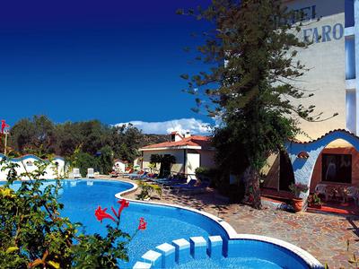 Hotel s modrým bazénem, kvetoucími květinami a jasnou oblohou v pozadí.