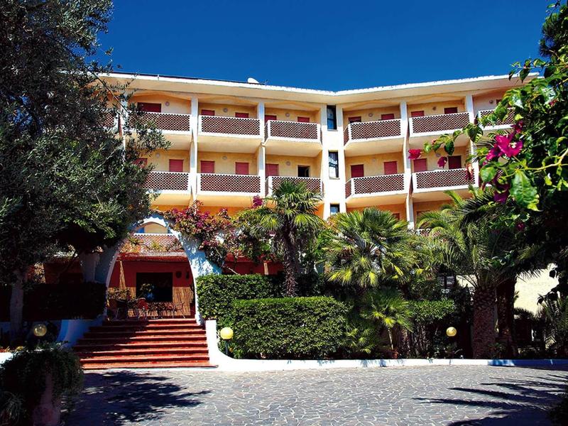 Mehrstöckiges Hotel mit Balkonreihen, roter Treppe und üppigem Grün vor blauem Himmel.