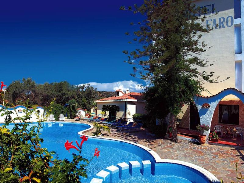 Runder Pool mit blauem Wasser, umgeben von Pflanzen und Gebäuden unter klarem Himmel.