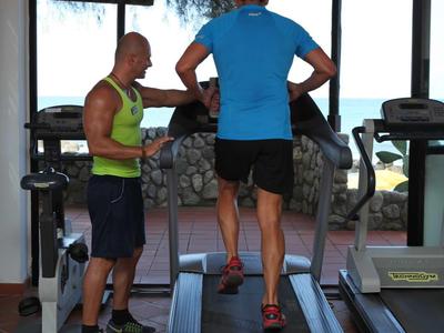 Dos hombres en un gimnasio, uno corre en la cinta mientras el otro observa.