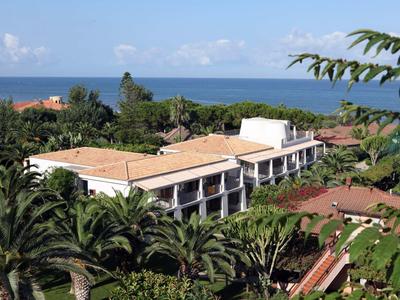 Edificio del hotel con techos rojos, rodeado de palmeras y vista al mar al fondo.