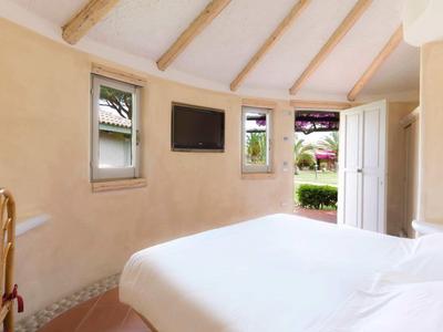 Przytulny pokój hotelowy z białymi ścianami, podwójnym łóżkiem i widokiem na ogród.