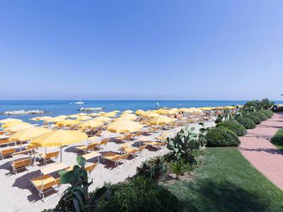 Plaża z licznymi żółtymi parasolami i leżakami pod jasnym niebieskim niebem.