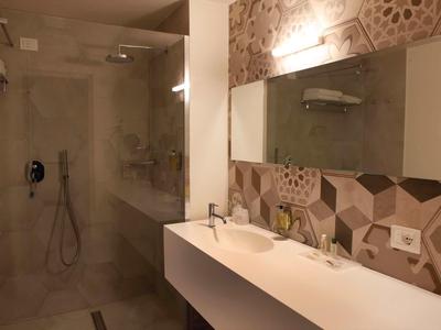 Nowoczesna łazienka z dużym prysznicem typu walk-in, podwójnymi umywalkami i geometrycznym wzorem na ścianie.