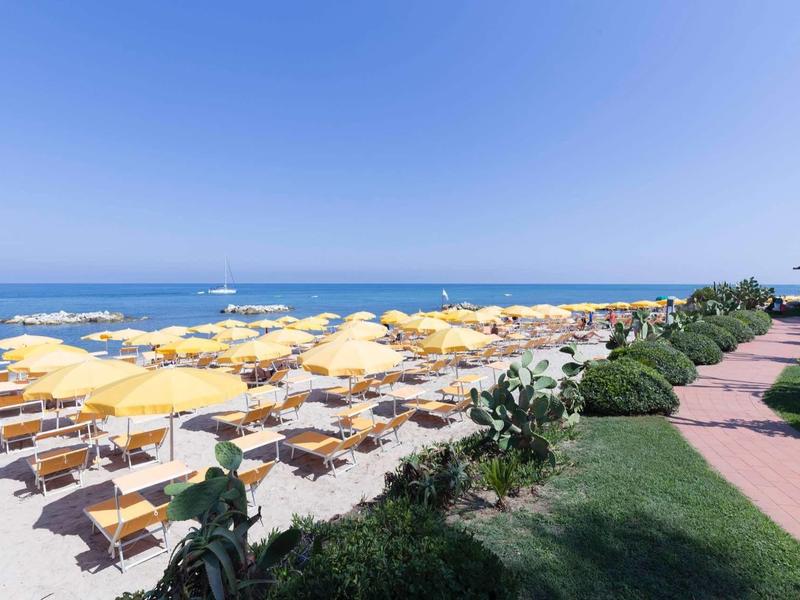 Plaża z licznymi żółtymi parasolami i leżakami pod jasnym niebieskim niebem.