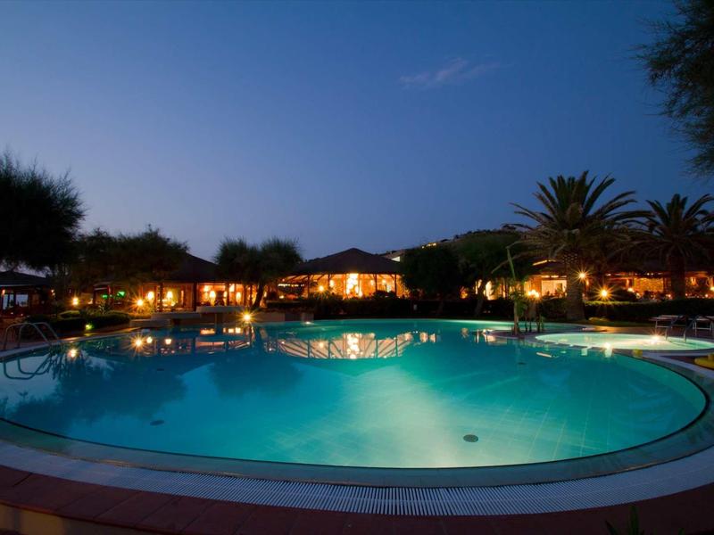 Oświetlony hotelowy basen nocą z palmami i spokojną atmosferą.