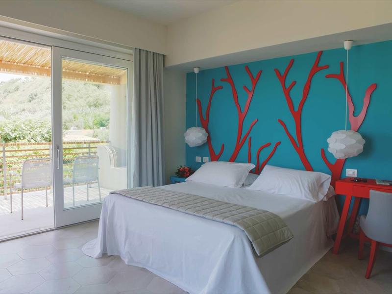 Nowoczesny pokój hotelowy z łóżkiem dwuosobowym, kolorowym wzorem na ścianie i balkonem z stołem i krzesłami.