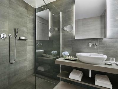 Bagno d'hotel moderno con doccia walk-in, grande specchio e lavabo su mensola in legno.