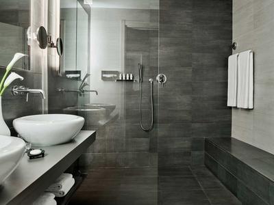 Bagno moderno con doccia a filo pavimento, lavabi e piastrelle grigie.