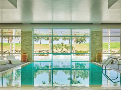 Piscina interna con lettini e grande finestra con vista su giardino e lago.