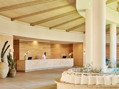 Reception dell'hotel con bancone bianco, piante e ambiente moderno e luminoso.