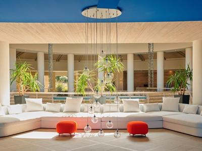 Area lounge d'hotel moderna con divani bianchi, sgabelli rossi e piante sotto il cielo azzurro.