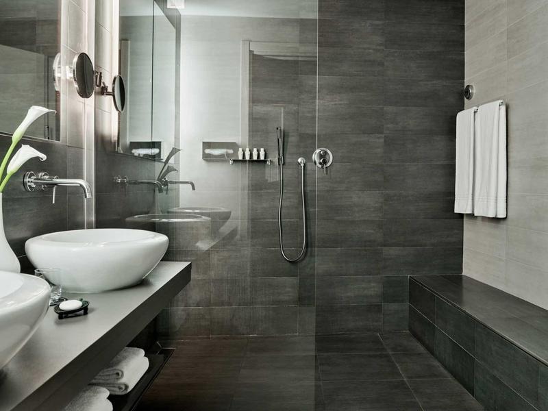 Bagno moderno con doccia a filo pavimento, lavabi e piastrelle grigie.