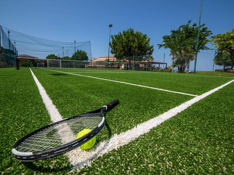 Campo da tennis con erba sintetica verde, racchetta da tennis e pallina sulla linea.