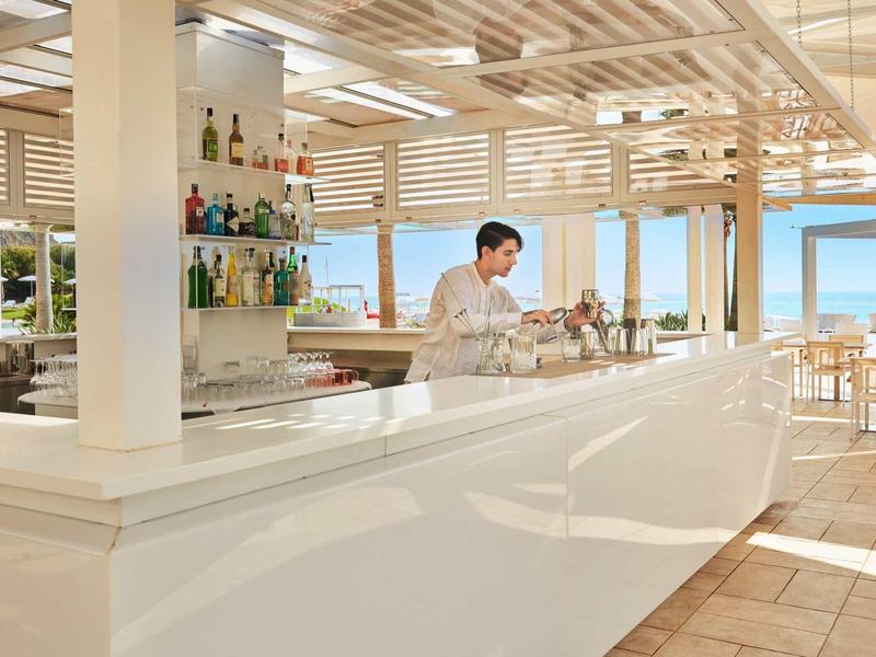 Area bar moderna dell'hotel con barman e vista sul mare alla luce del giorno.