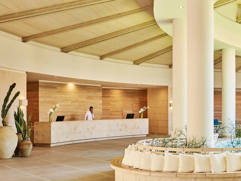 Reception dell'hotel con bancone bianco, piante e ambiente moderno e luminoso.