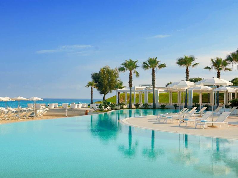 Piscina a sfioro con palme e ombrelloni bianchi con vista sul mare