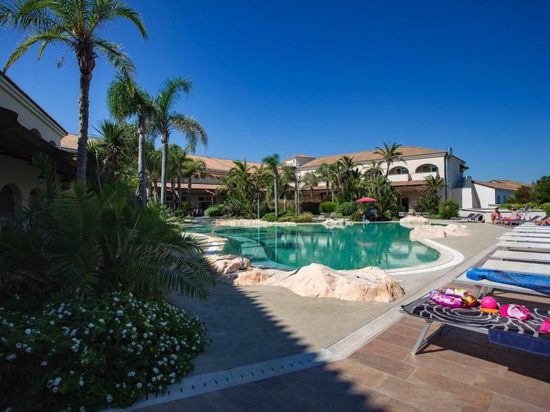 Basen hotelowy z leżakami, palmami i bezchmurnym niebem w ośrodku wakacyjnym.