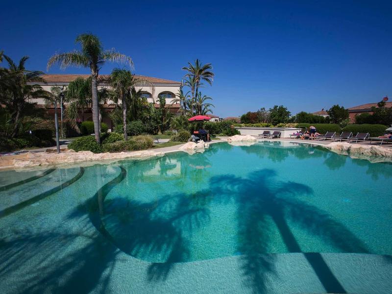 Przejrzysty basen z palmami i leżakami pod niebieskim niebem w hotelowym kurorcie.