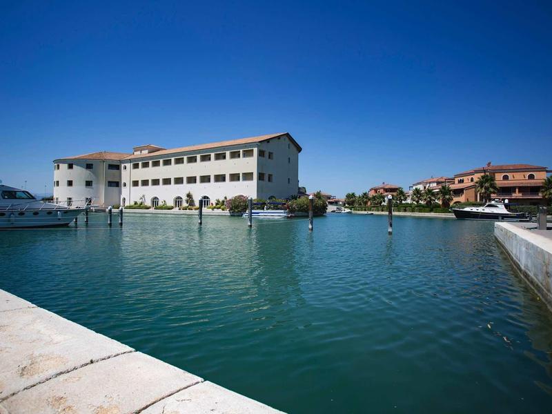 Duży budynek hotelu obok spokojnej wody pod jasnym niebieskim niebem.