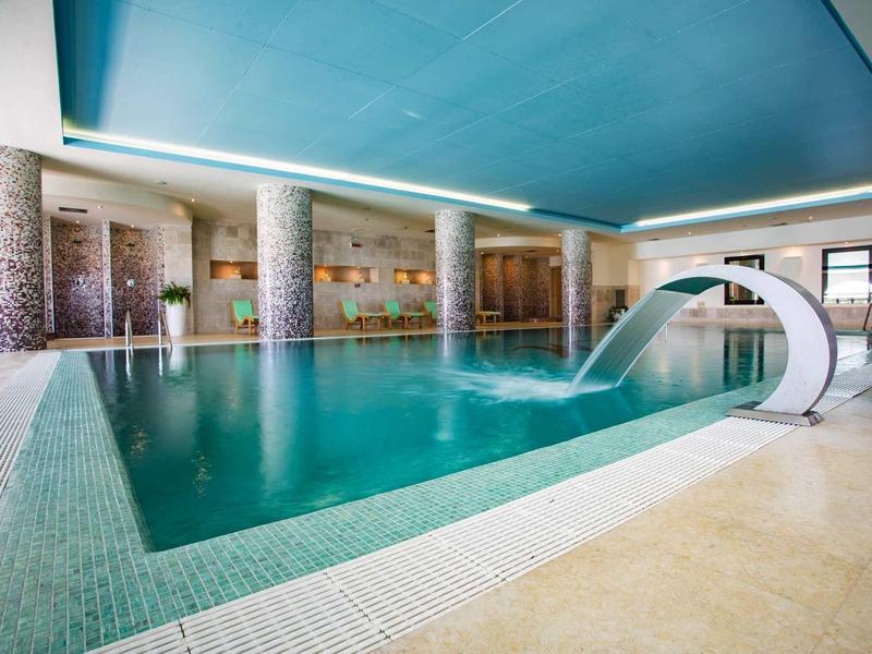 Basen kryty z niebieskim sufitem, zjeżdżalnią wodną i marmurowanymi kolumnami.
