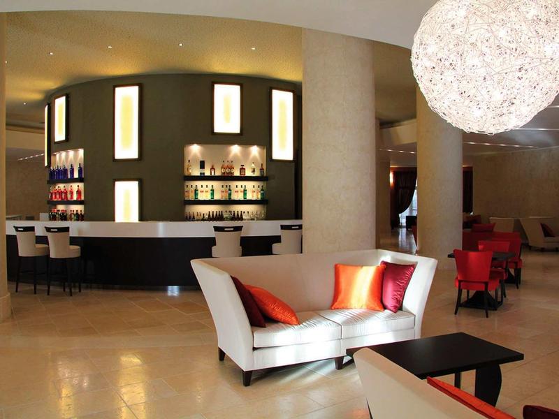 Nowoczesna lobby hotelowa z białymi sofami, kolorowymi poduszkami i stylowym oświetleniem.