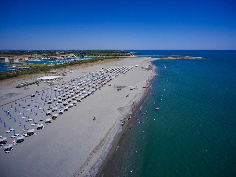 Rozległa piaszczysta plaża z rzędami parasoli i czystą niebieską wodą pod niebieskim niebem.