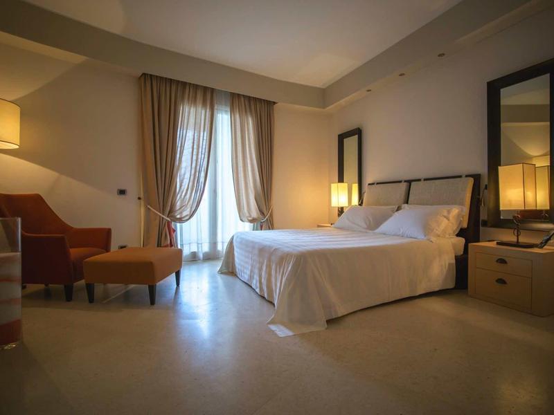 Przytulny pokój hotelowy z podwójnym łóżkiem, fotelem i miękkim oświetleniem o zmierzchu.