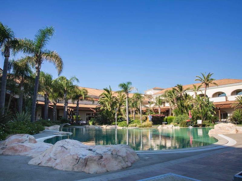 Hotel z dużym basenem otoczonym palmami i czystym niebieskim niebem.