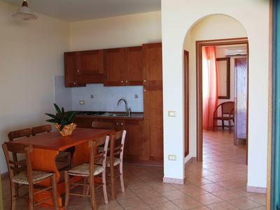 Piccola angolo cottura con mobili in legno e tavolo da pranzo in una stanza luminosa con pavimento piastrellato.