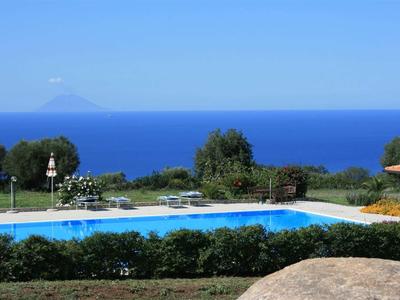 Ein Pool mit Blick auf das Meer und einen Berg am Horizont unter blauem Himmel.