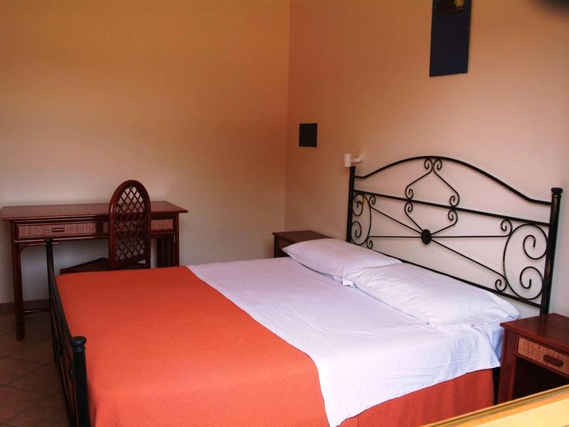 Camera d'hotel semplicemente arredata con letto matrimoniale, scrivania e sedia.