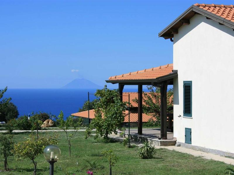 Casa bianca con tetto rosso e terrazza con vista sul mare e una montagna lontana.