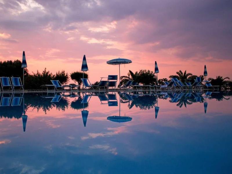 Tramonto su una piscina tranquilla con lettini e ombrelloni.