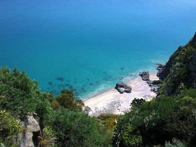 View from above of a small sandy beach with clear blue water, surrounded by rocks and green vegetation.