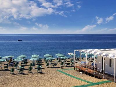 Beach with rows of umbrellas and a small white hut by the sea.