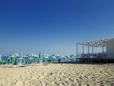 Expansive sandy beach with green umbrellas and a white beach building under a blue sky.