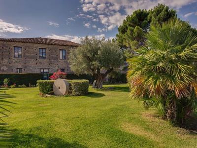 Stone house with manicured garden and palm trees under a blue sky with clouds