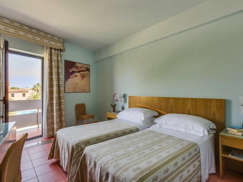 Brightly furnished hotel room with two single beds and a balcony with an outdoor view.
