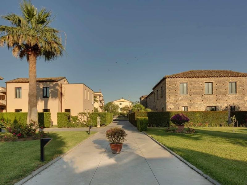 View of a walkway between hotel buildings with palm trees and well-maintained lawns under clear sky.