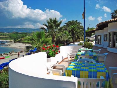 Terrasse mit bunten gedeckten Tischen und Blick auf Strand und Palmen bei bewölktem Himmel