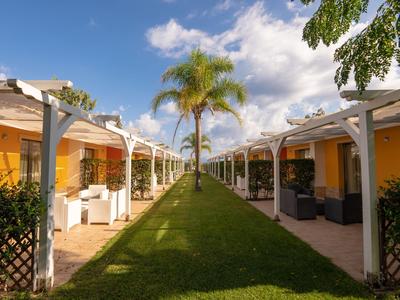 Área de jardín simétrica con césped verde, palmeras y bungalows amarillos del hotel.