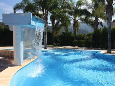 Piscina moderna con cascata e palme in un'area esterna soleggiata.