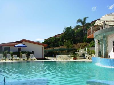 Hotelpoolbereich mit Liegestühlen, Sonnenschirmen und begrünten Hügeln im Hintergrund.