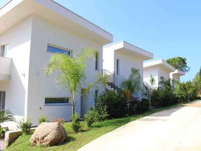 Fila di moderne case vacanza bianche con giardini e palme sotto un cielo terso.